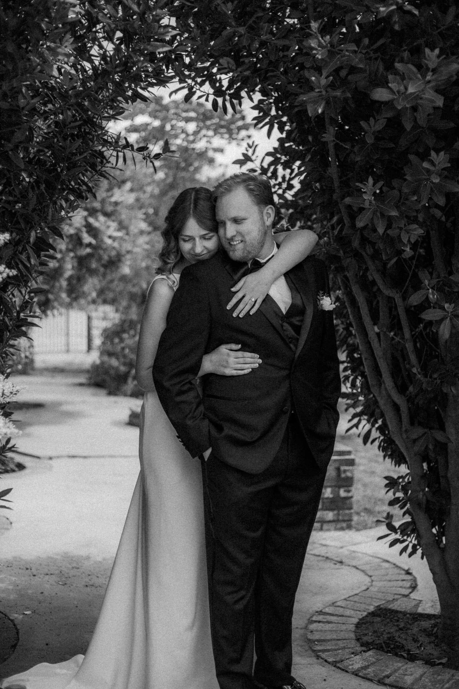 Blake and Ava embracing beneath a leafy arch, in black and white