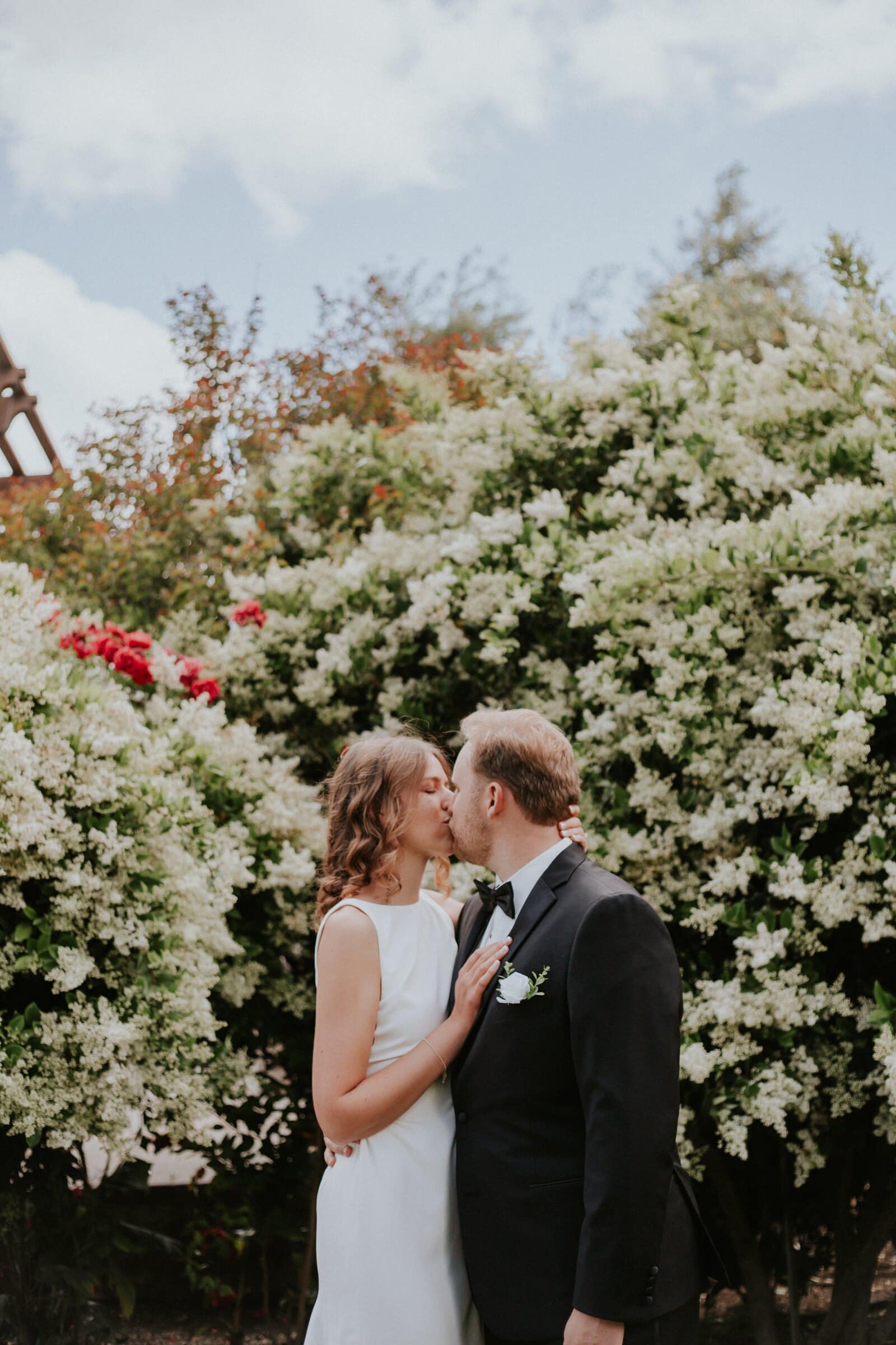 Blake and Ava kissing in front of white flowering shrubs