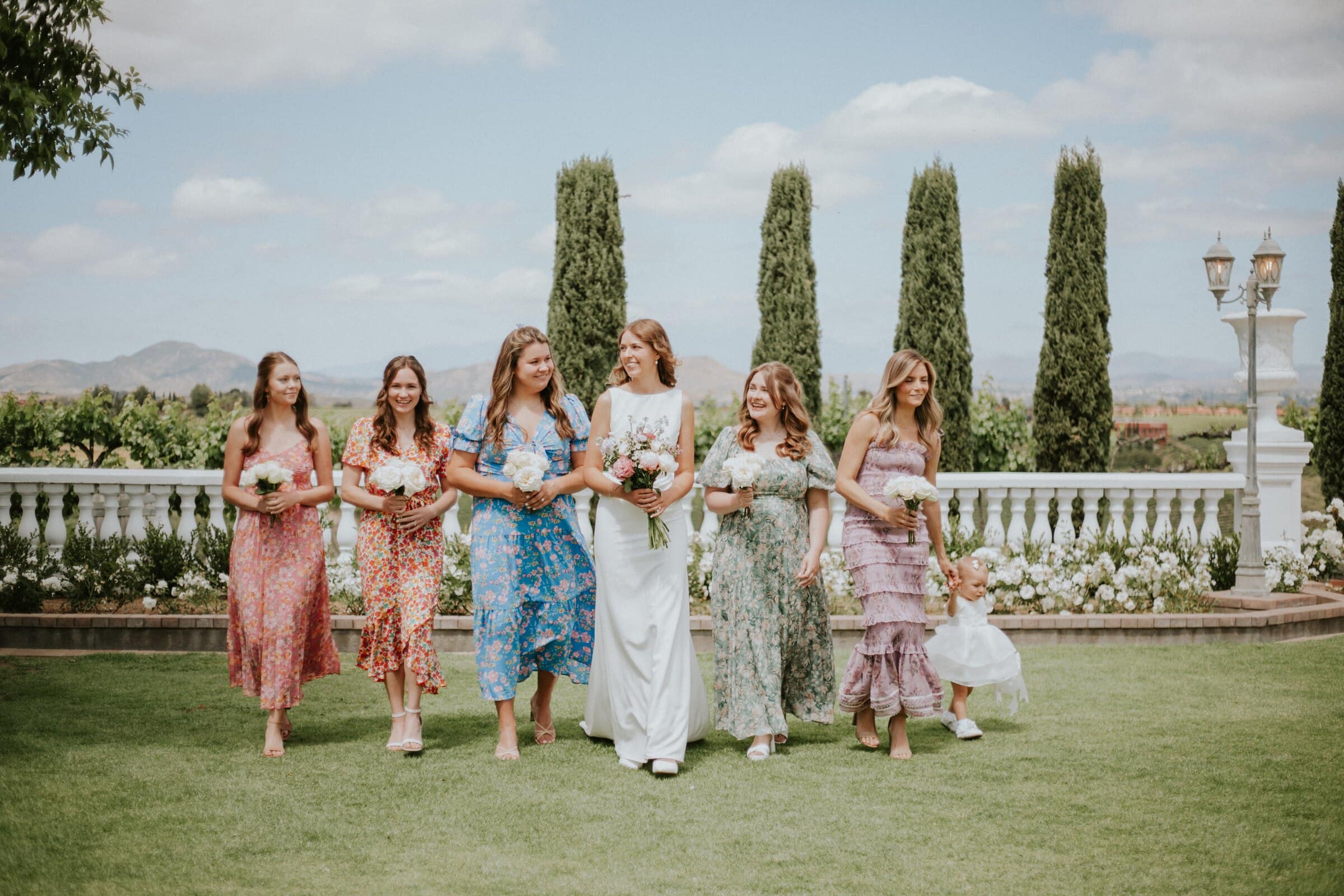 The bride and her bridesmaids walking across the lawn among cypress trees