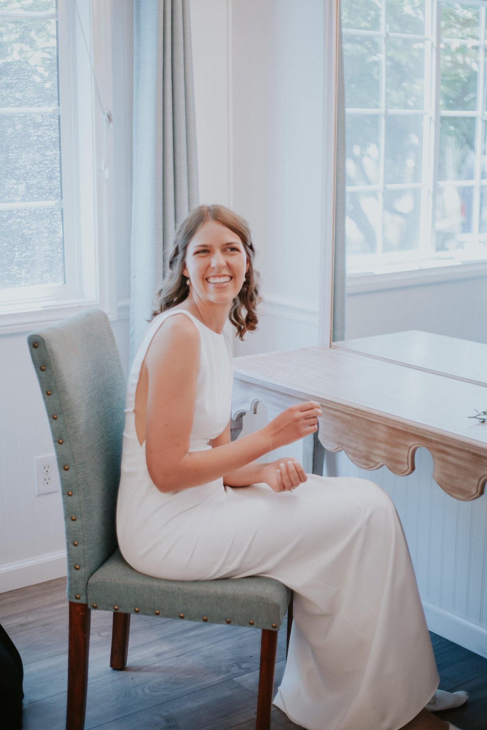 The bride sitting by a window in her gown