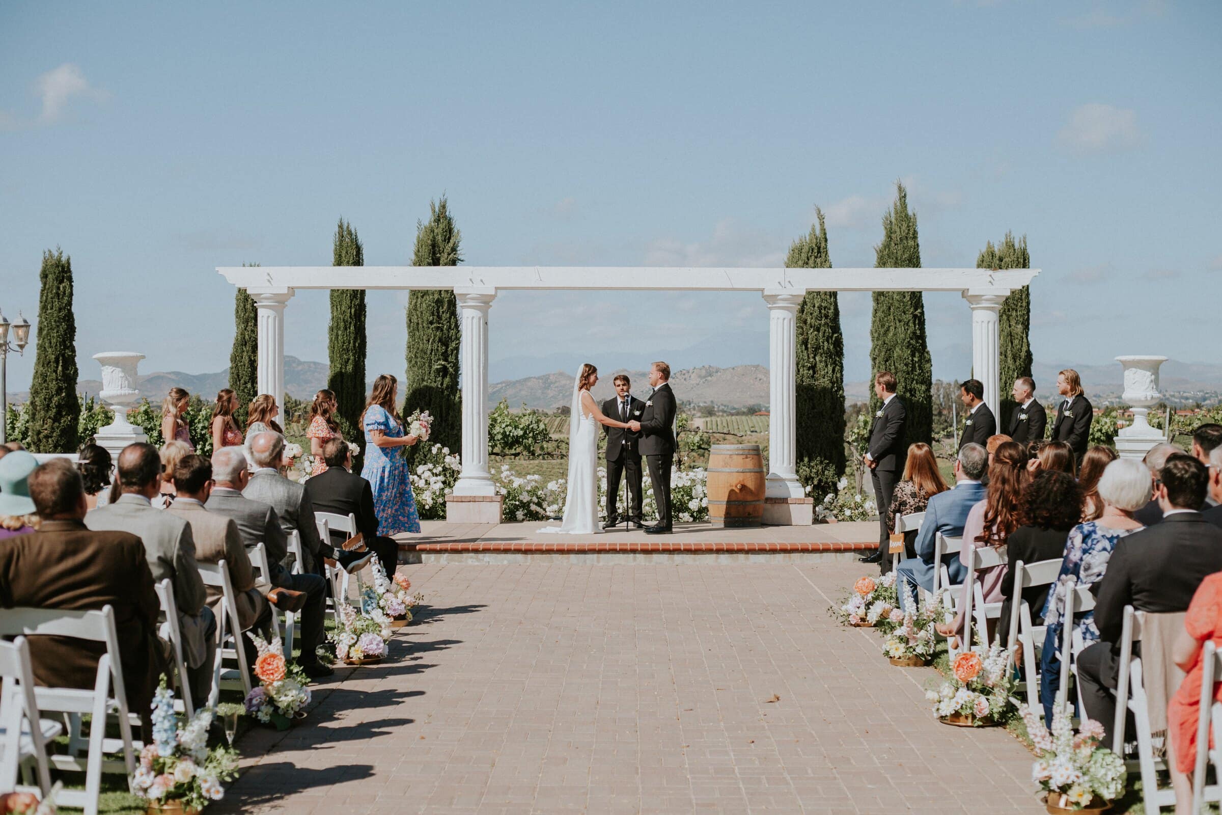 The ceremony seen from the back of the aisle, under a white colonnade with the hills beyond