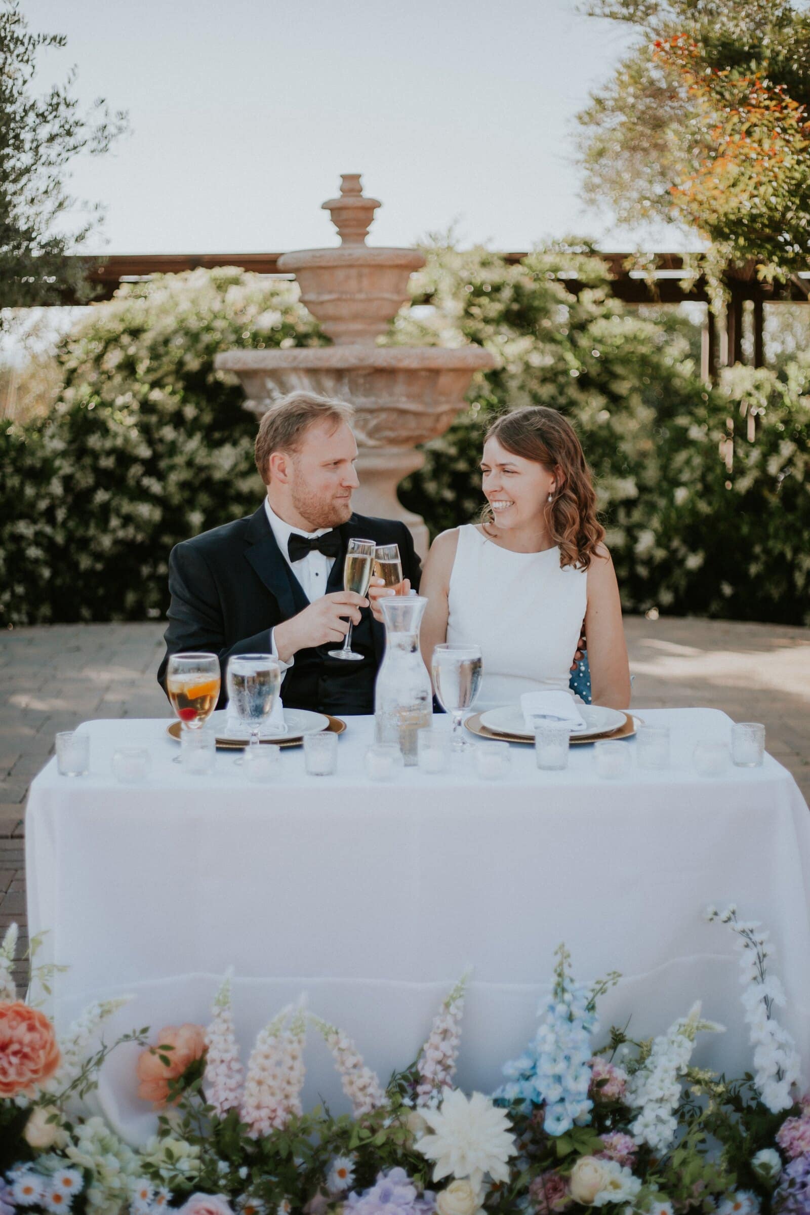 Blake and Ava raising a glass at their sweetheart table, surrounded by flowers