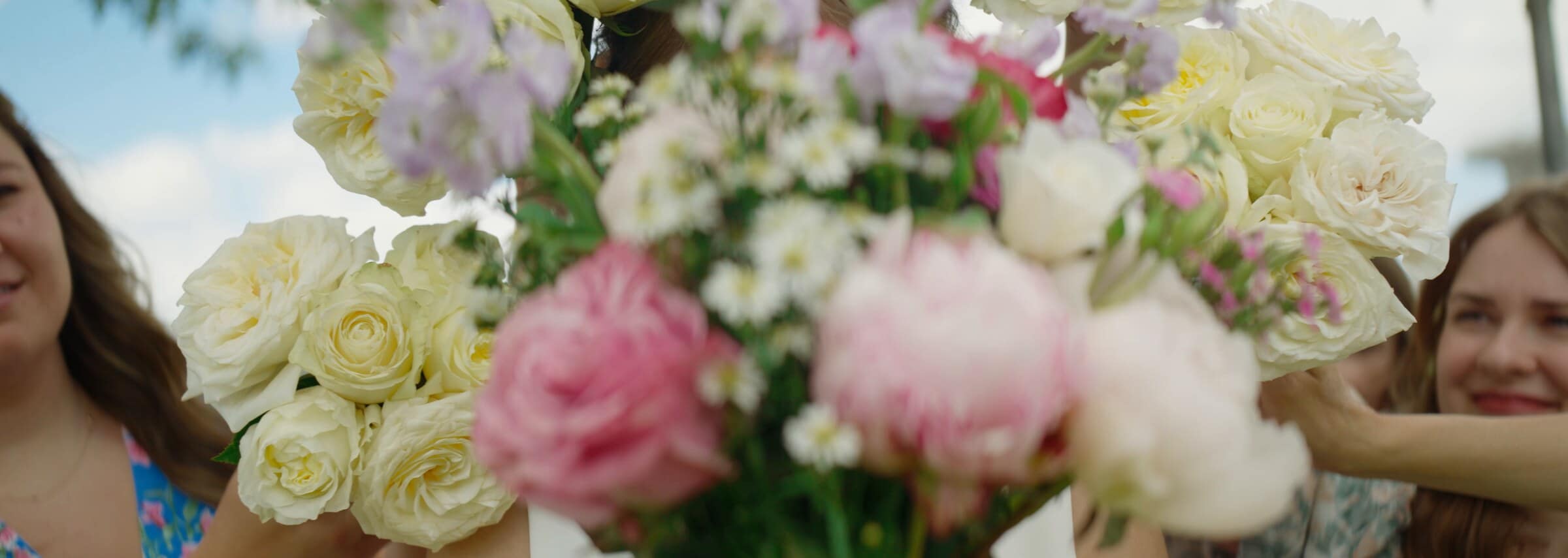 A bouquet of white and pink roses held up between bridesmaids