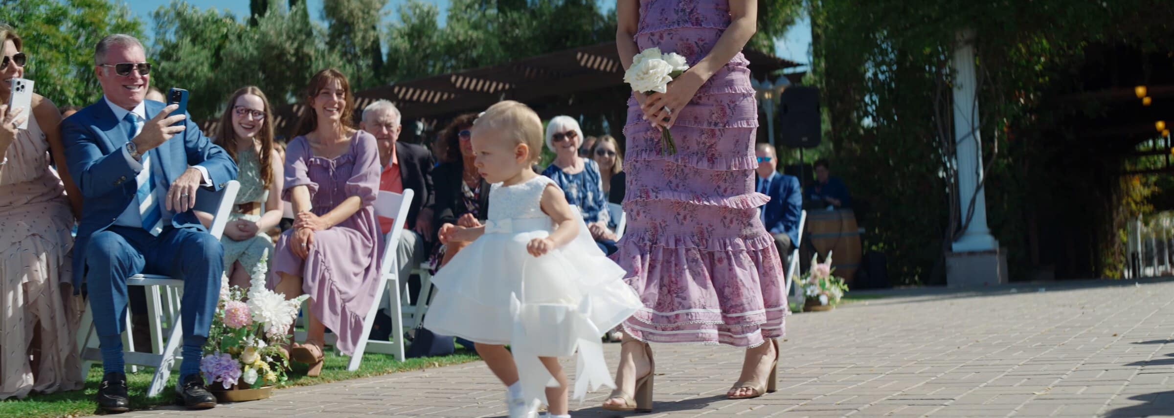 A flower girl in a white dress walking down the aisle