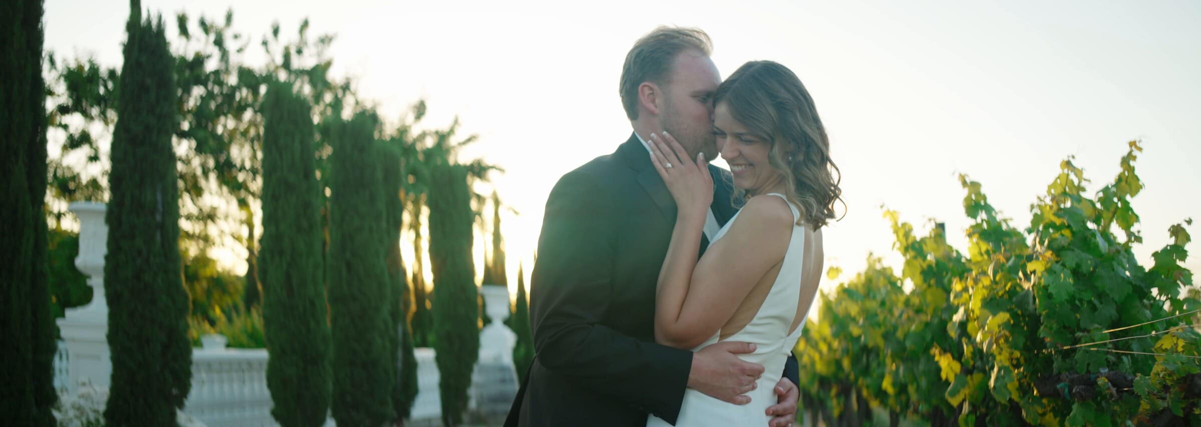 Blake and Ava holding each other at golden hour between cypress trees