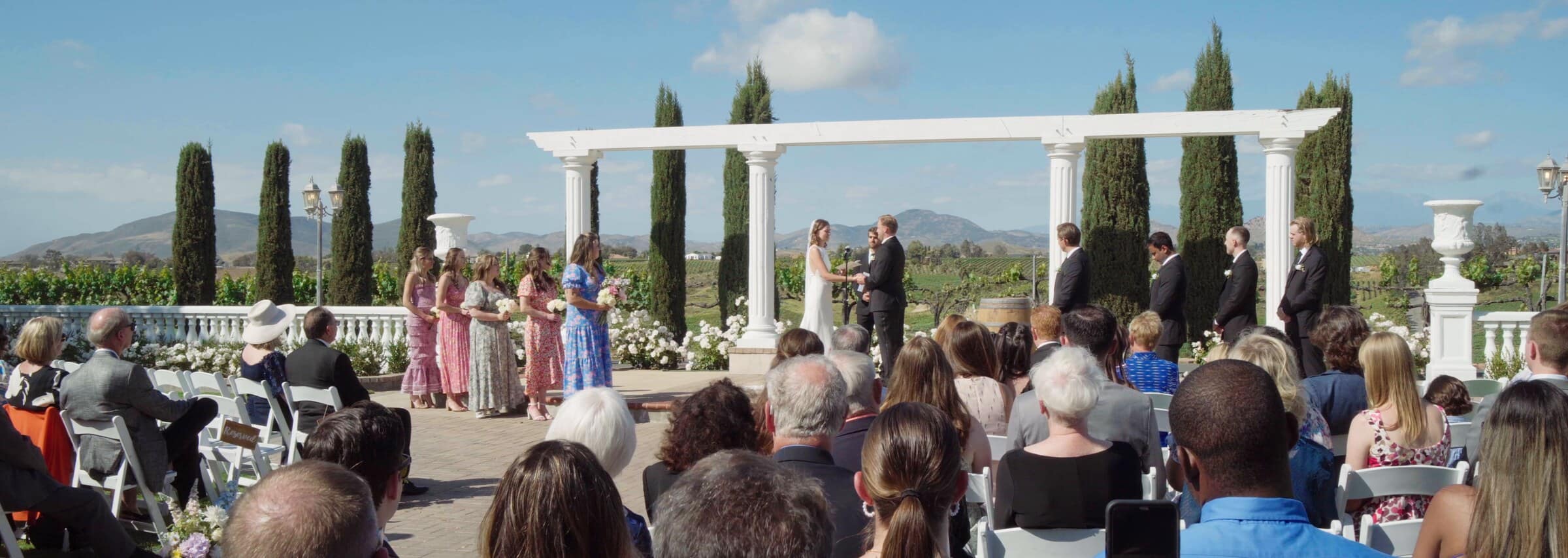 The ceremony under white columns and cypress trees, guests seated in front
