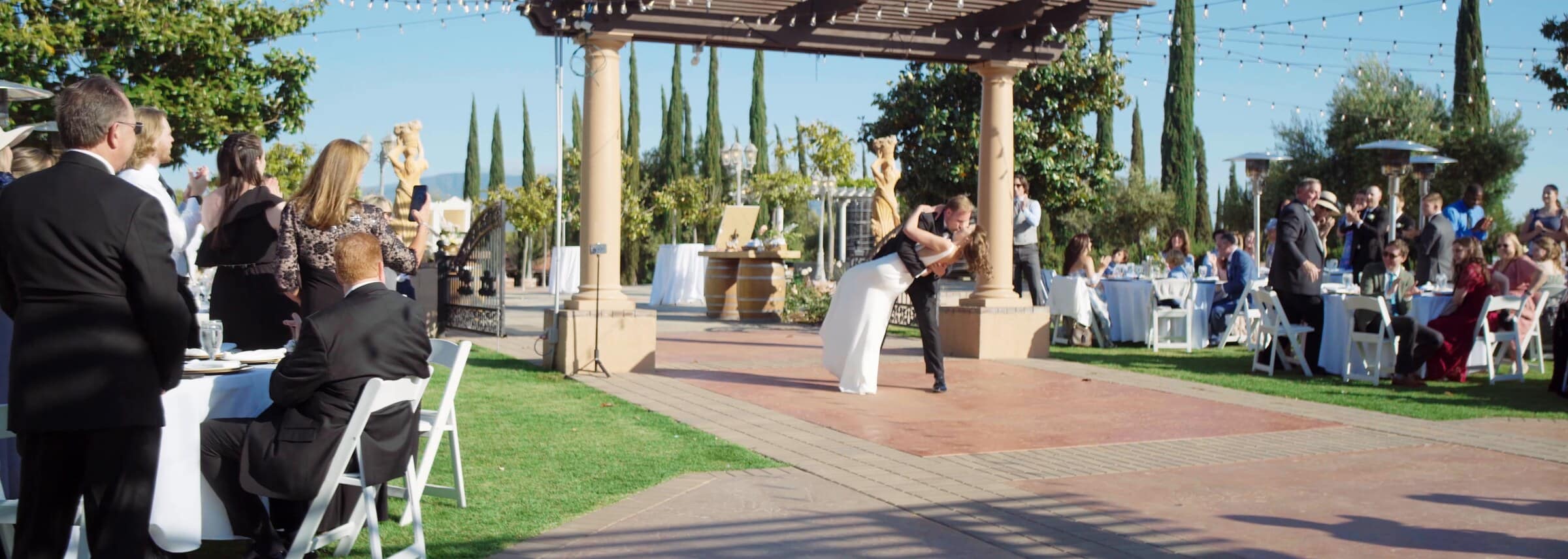 Blake and Ava dancing under a stone pergola as guests watch