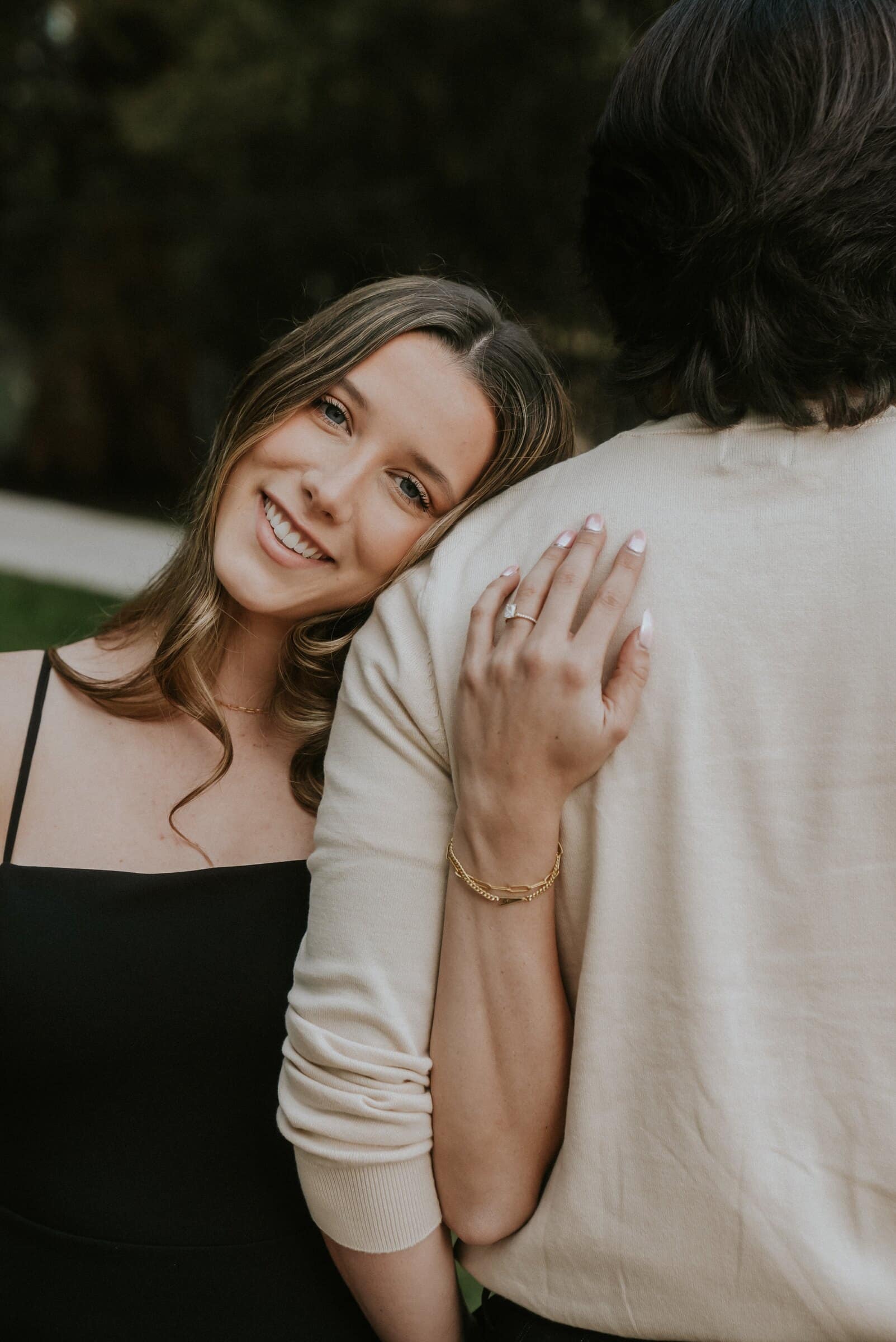 Amanda smiling over Cameron's shoulder, her ring hand on his arm