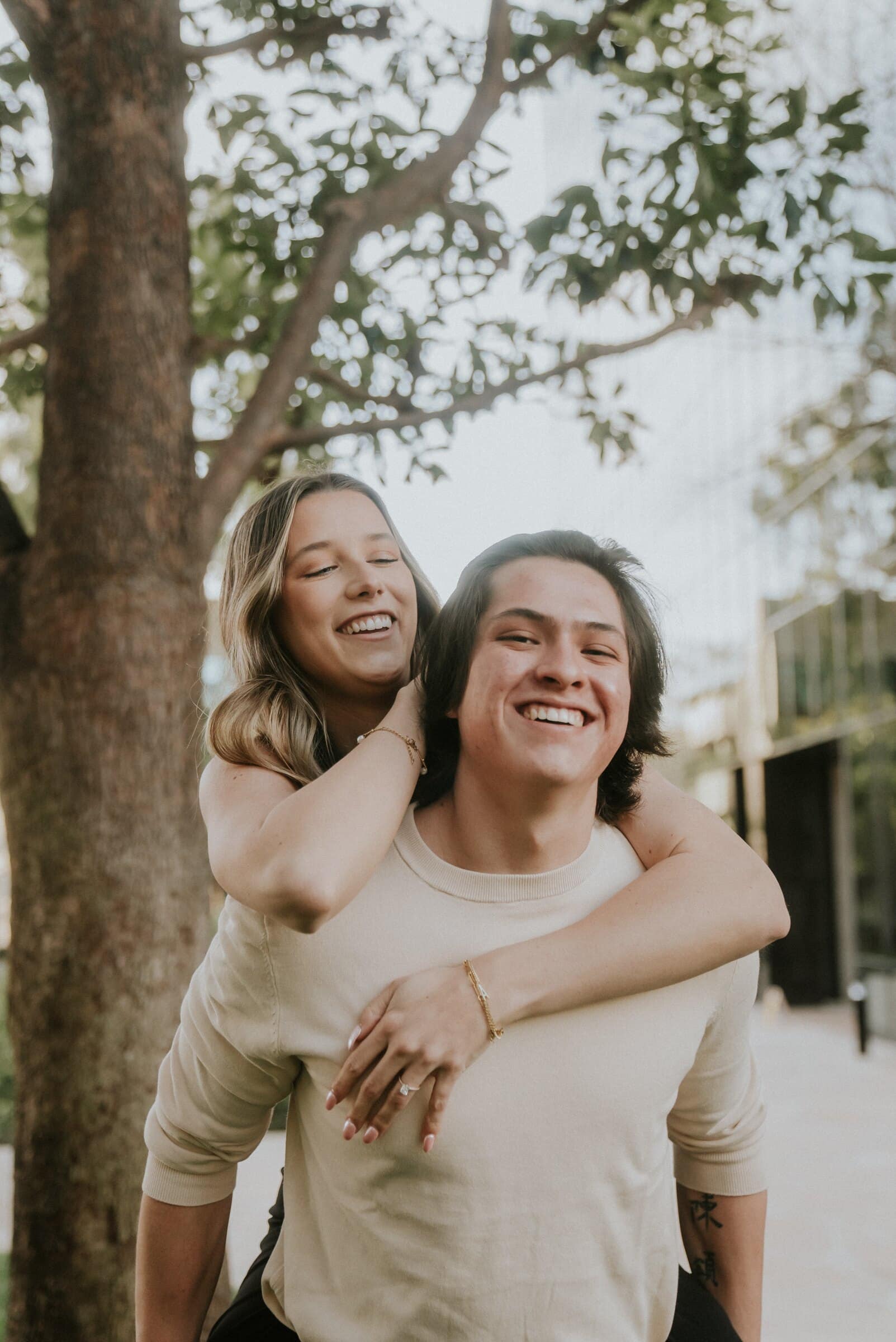 A piggyback ride under a tree, both grinning