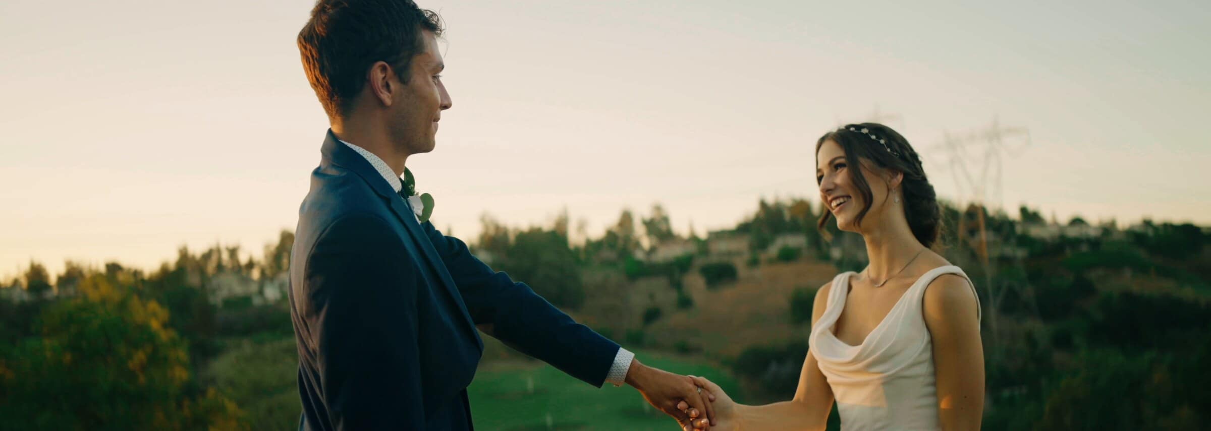 Claire and Bryce holding hands on a hilltop at golden hour