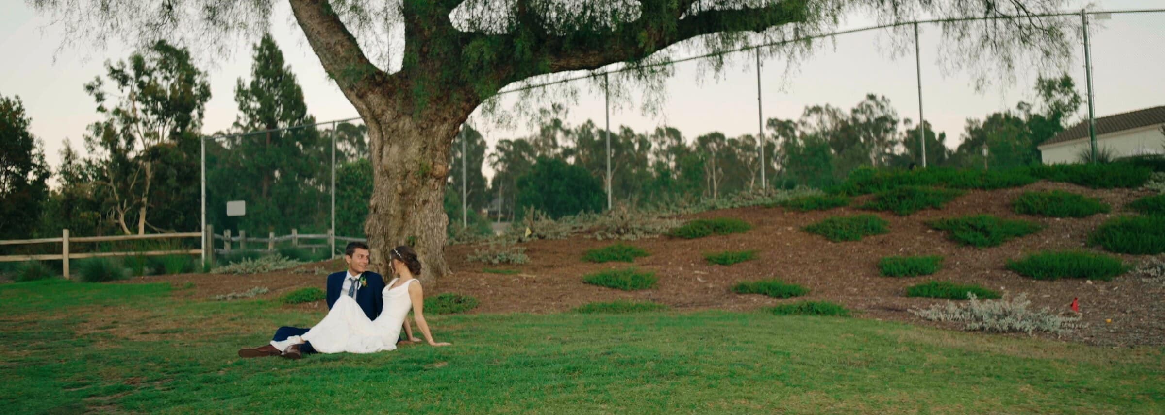 Claire and Bryce sitting in the grass beneath a huge old tree