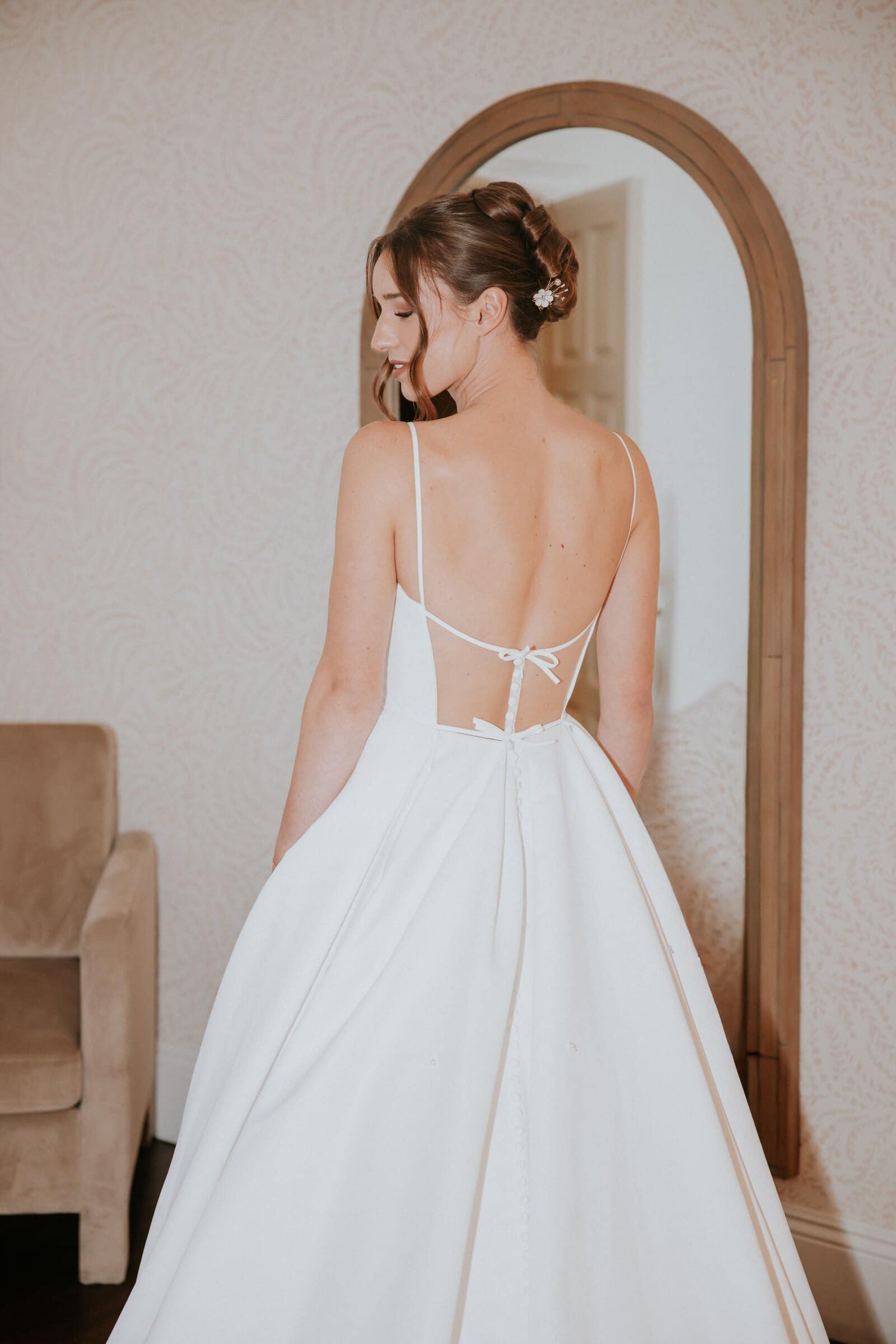 Clara in her gown in front of an arched mirror, seen from behind