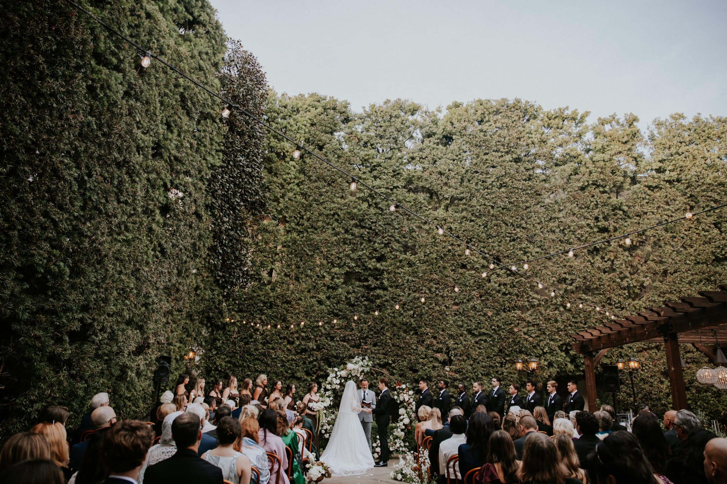 The ceremony in the ivy-walled courtyard, guests seated beneath the trees