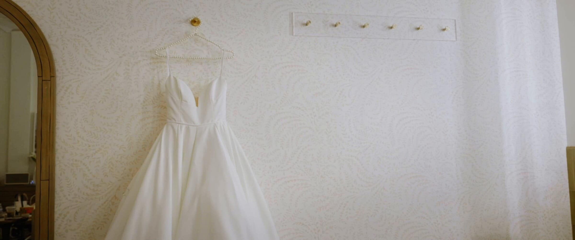 Clara's wedding dress hanging on a white wall