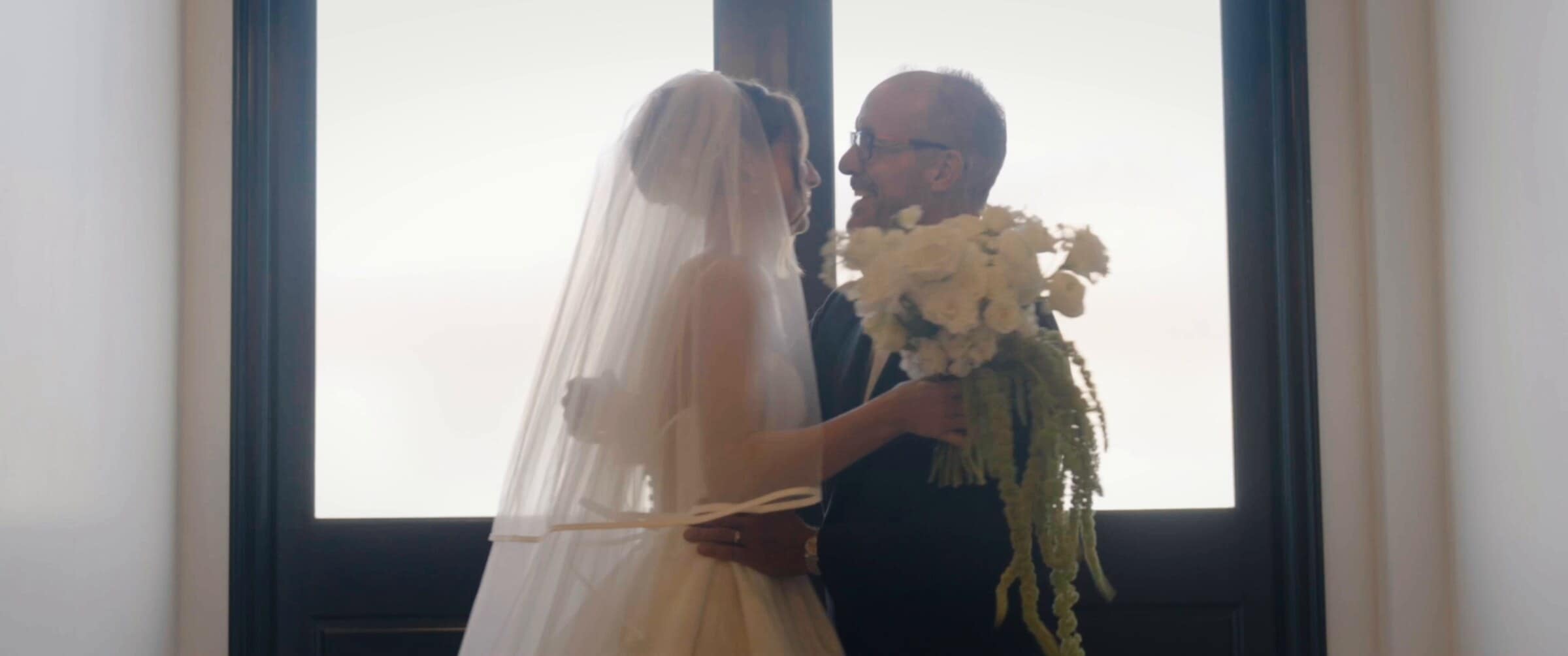 Clara sharing a quiet hug by a tall window before the ceremony