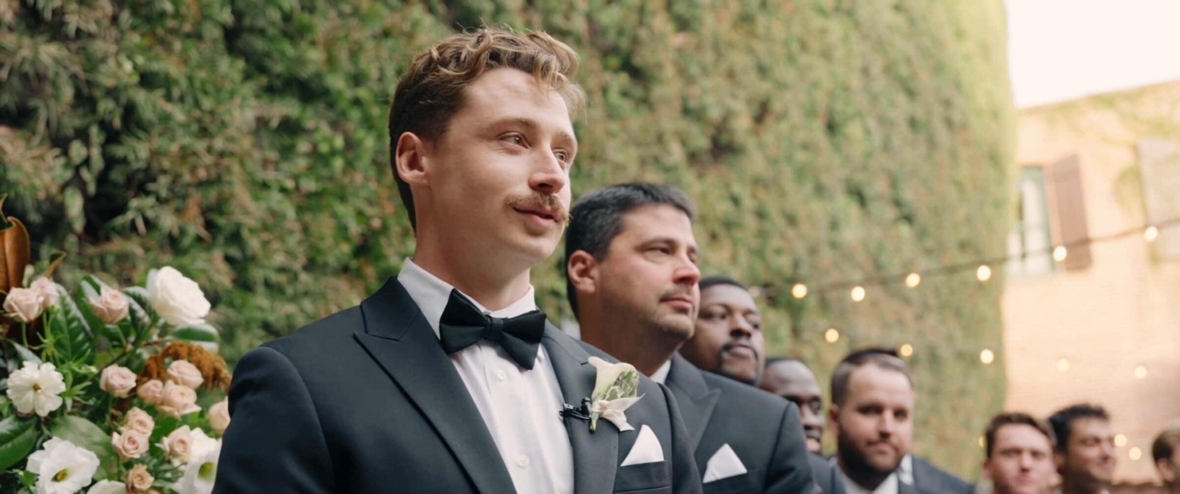 Grant watching Clara come down the aisle, his groomsmen behind him