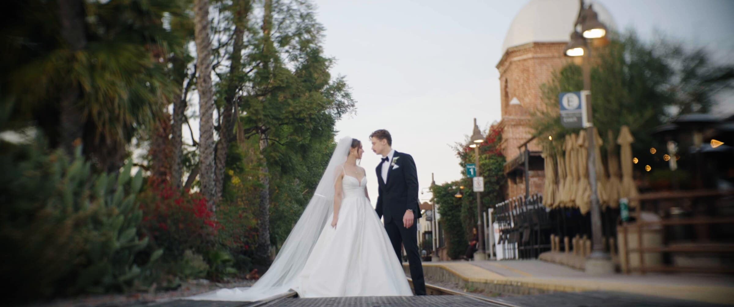 Clara and Grant on a quiet street at sunset, an old domed tower behind them