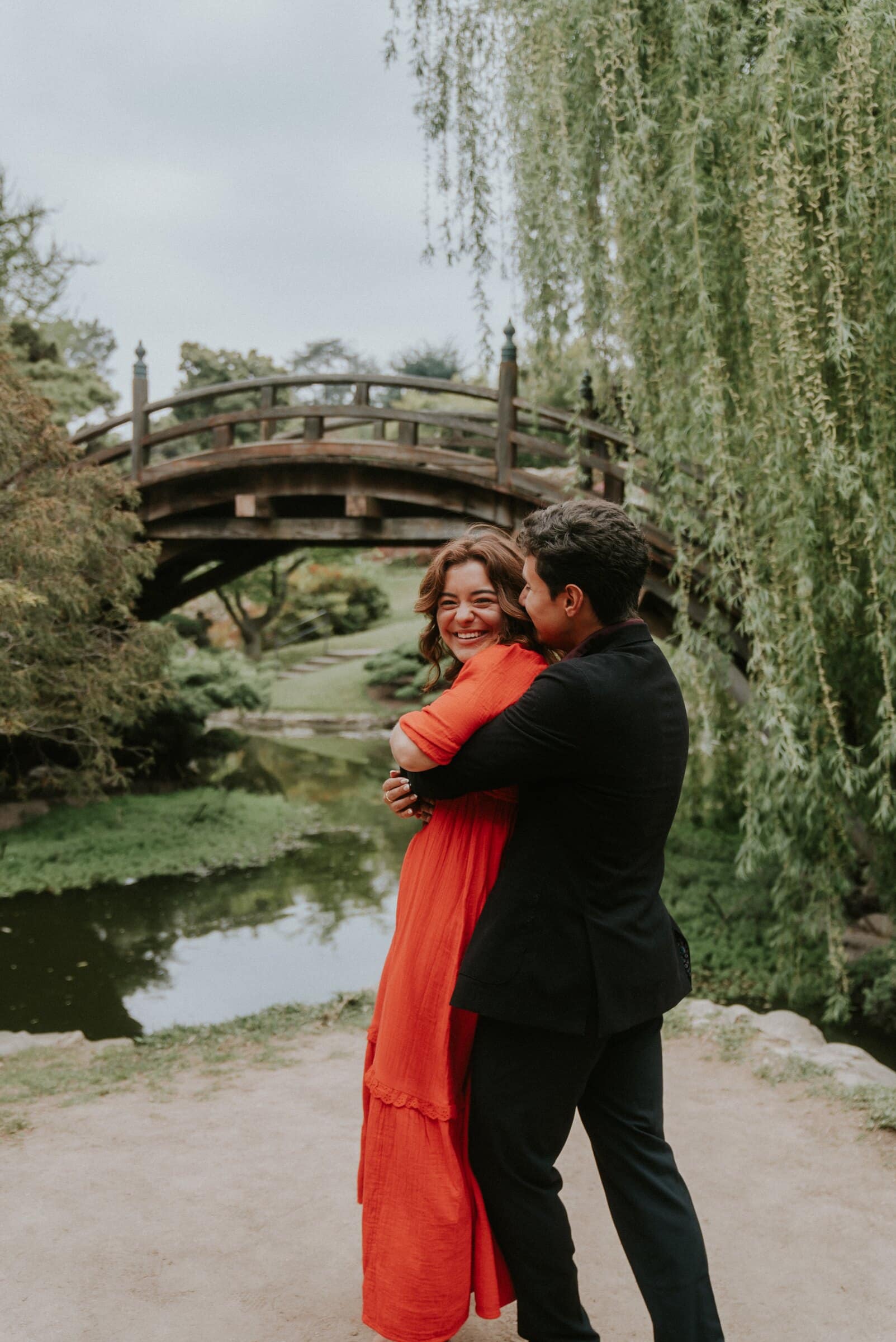 David and Natalie holding each other in front of an arched wooden bridge