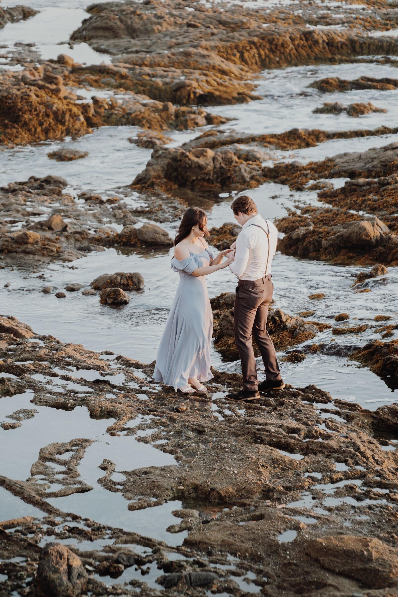 Dylan and Jasmine holding hands on the rocks after the proposal