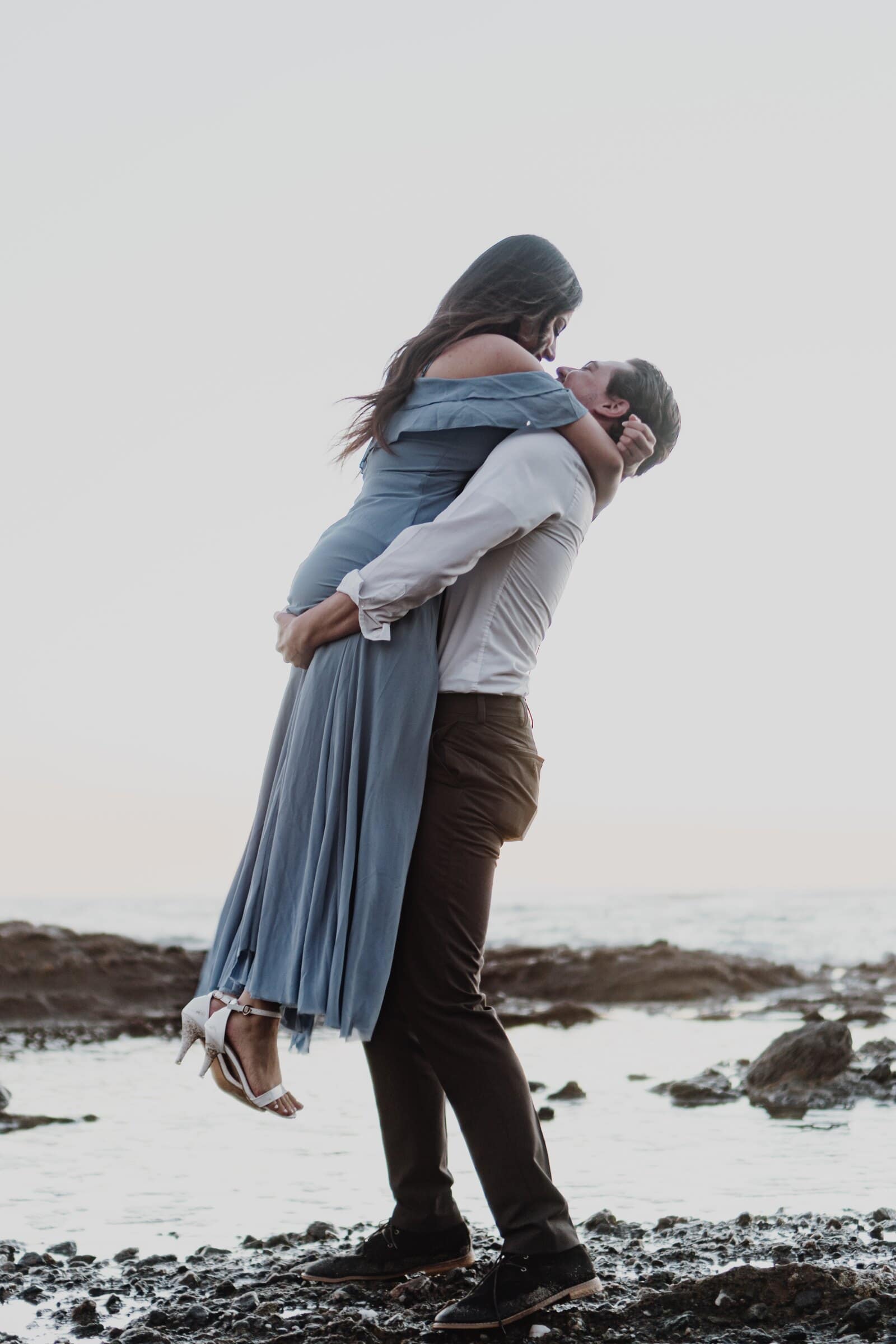 Dylan lifting Jasmine off her feet by the ocean