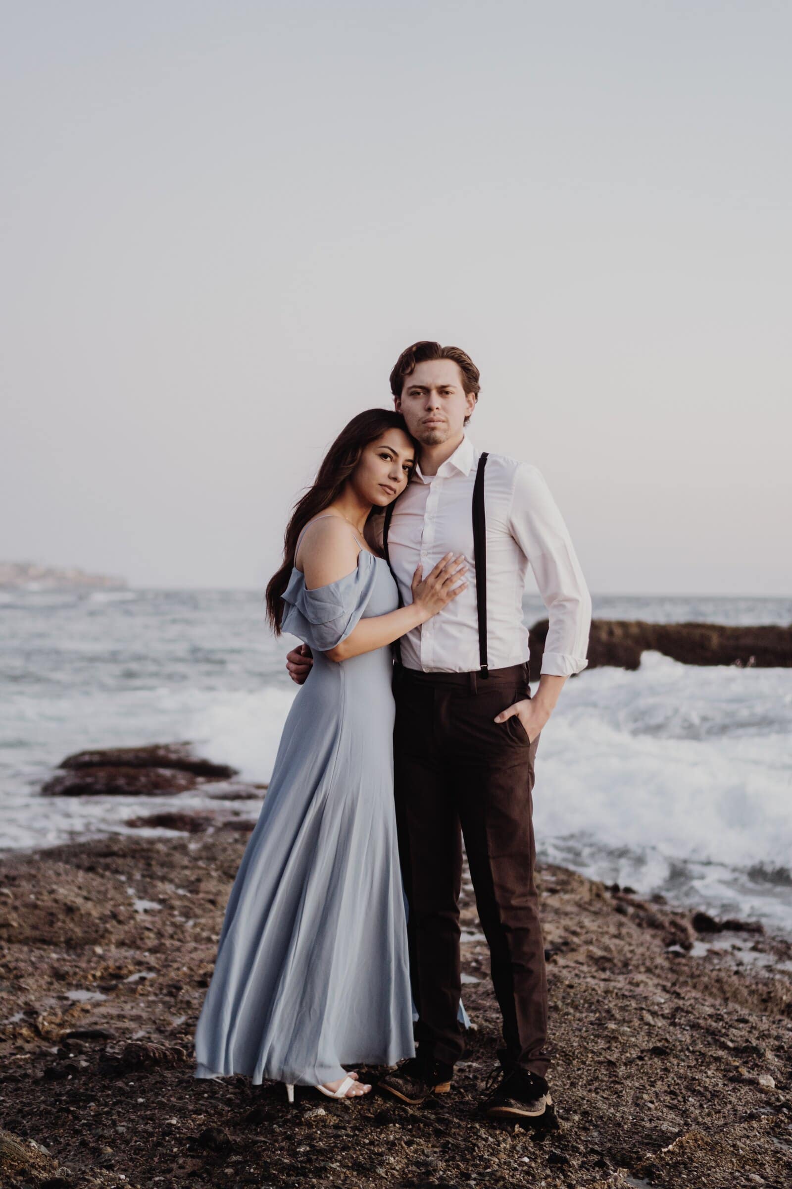 Dylan and Jasmine holding each other on the rocks, waves behind them
