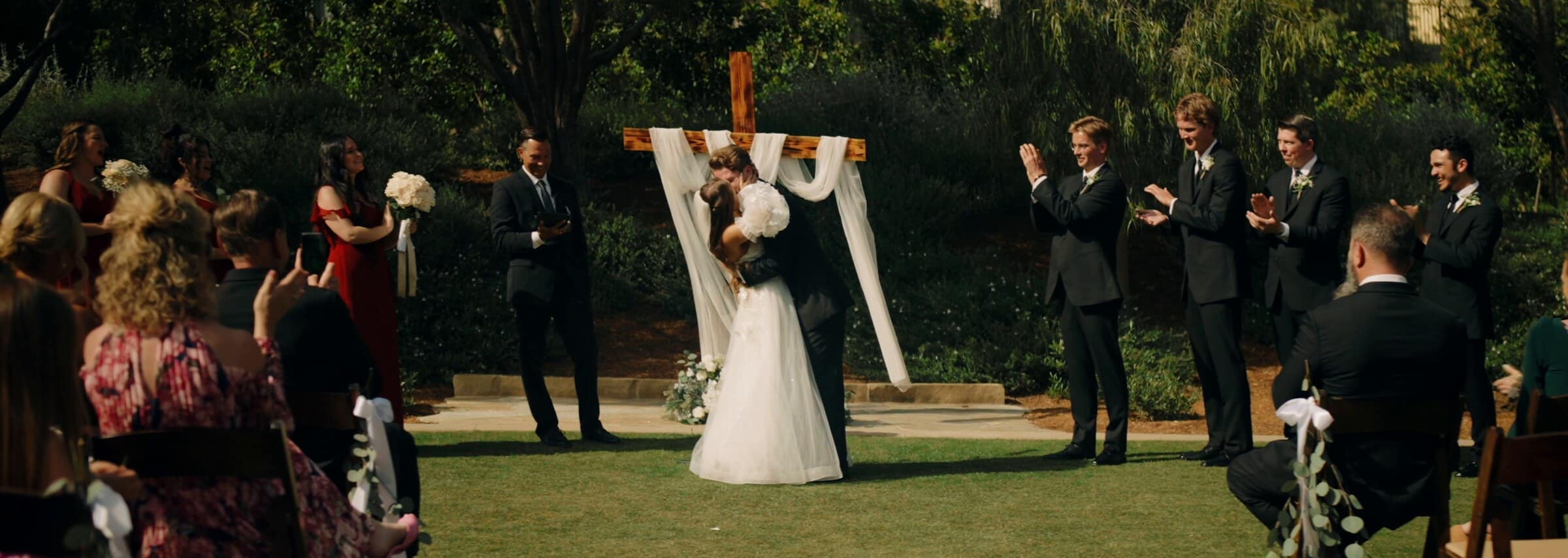 Irelyn and Aleck kissing at the altar beneath a wooden cross draped in white