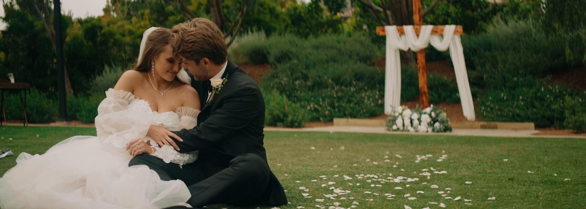 Irelyn and Aleck sitting together in the grass among scattered petals