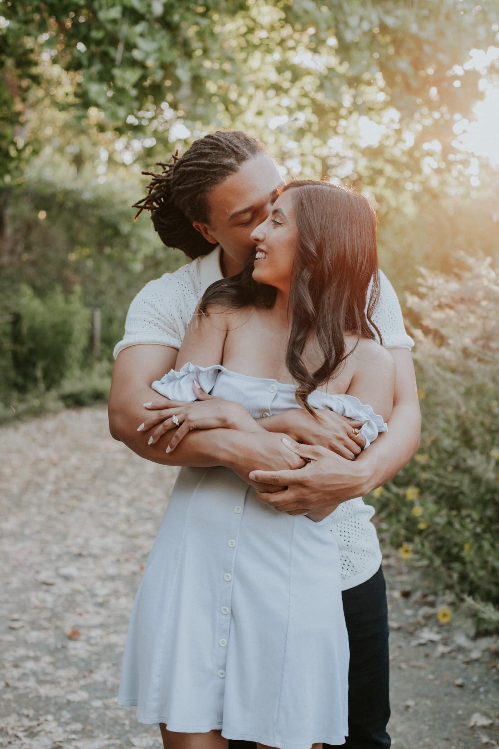 Jeremy kissing Ambica's cheek as he holds her from behind on a dirt path