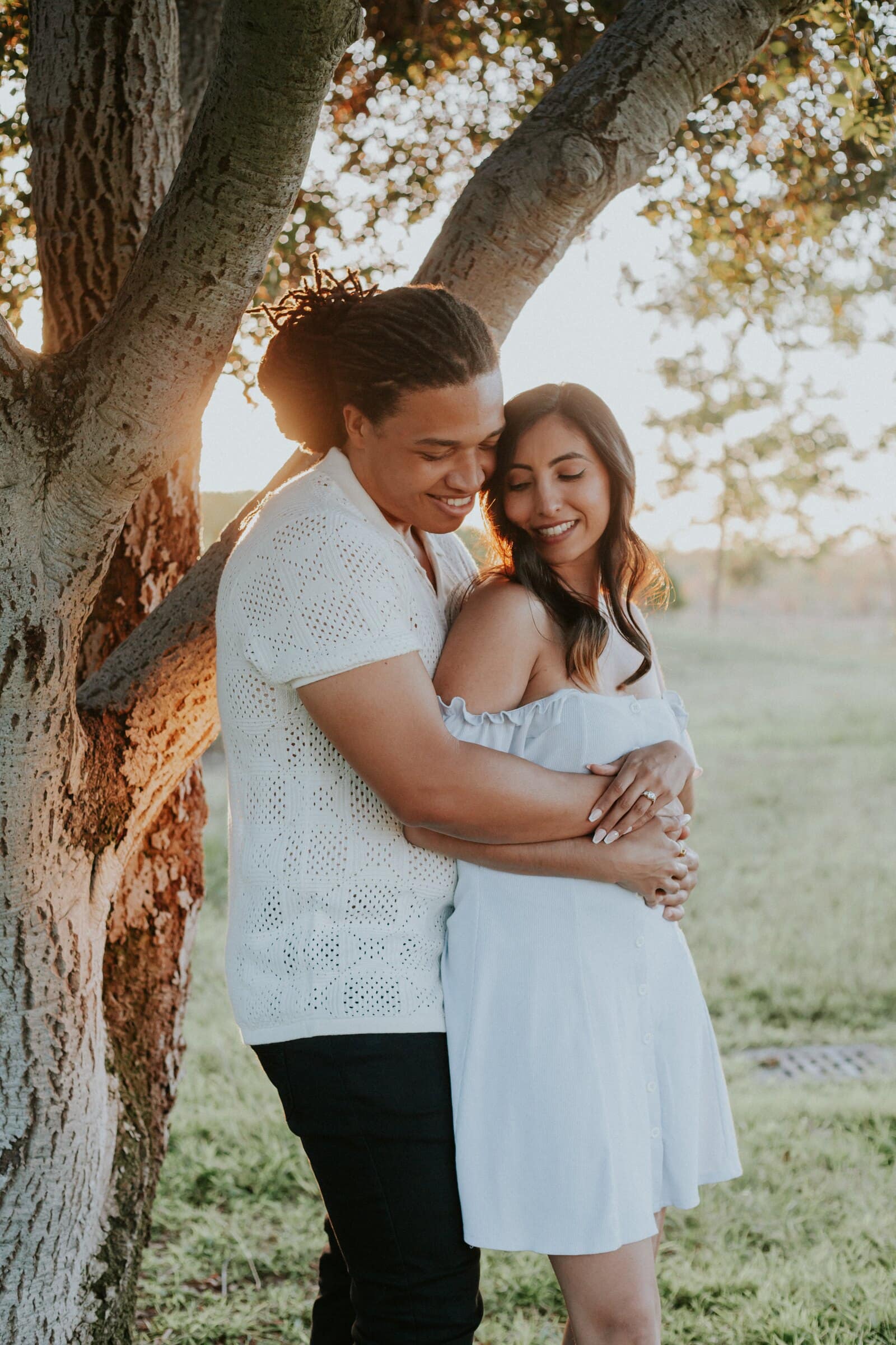 Jeremy and Ambica leaning against a tree trunk, his arms around her