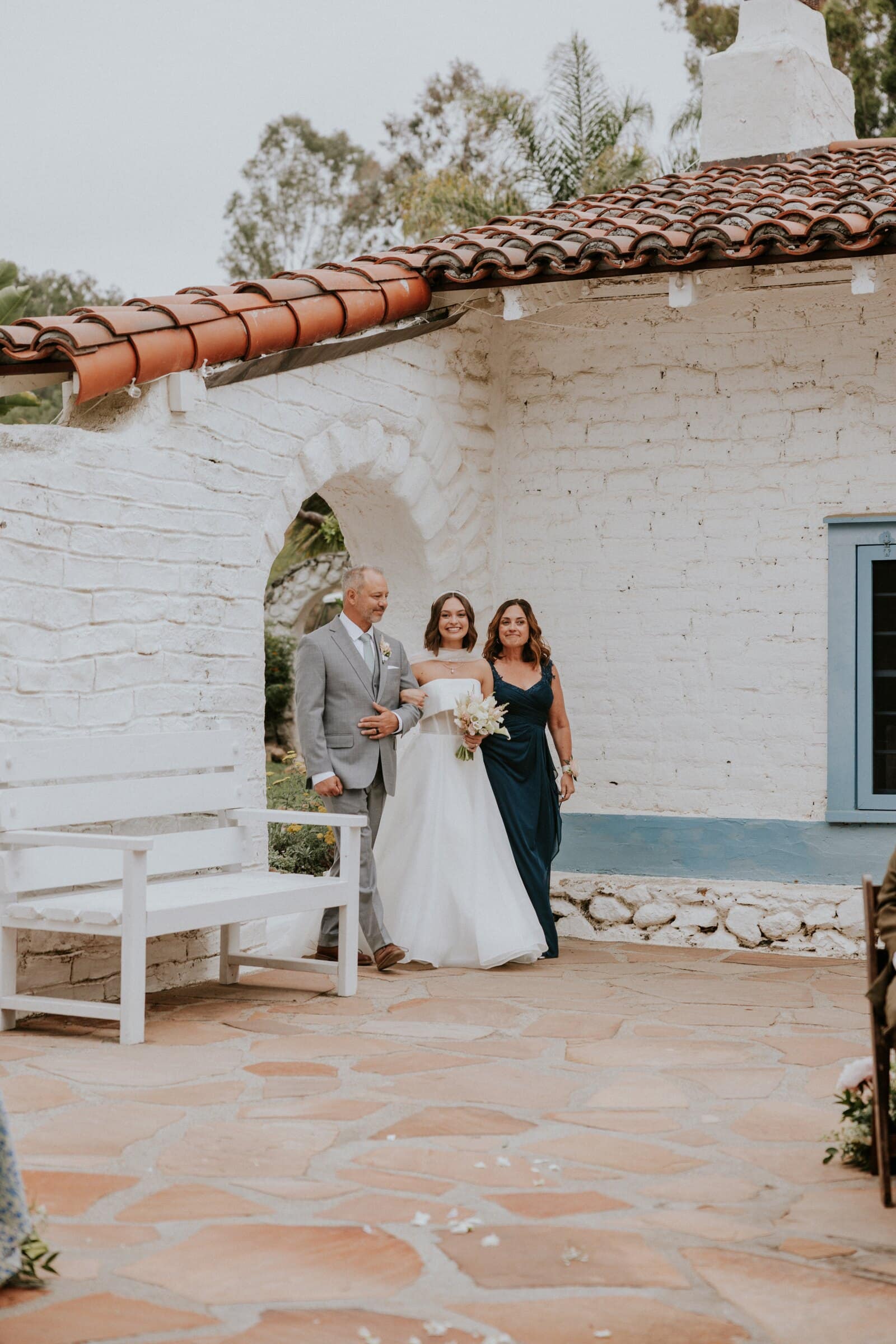 Megan walking toward the ceremony past a whitewashed adobe