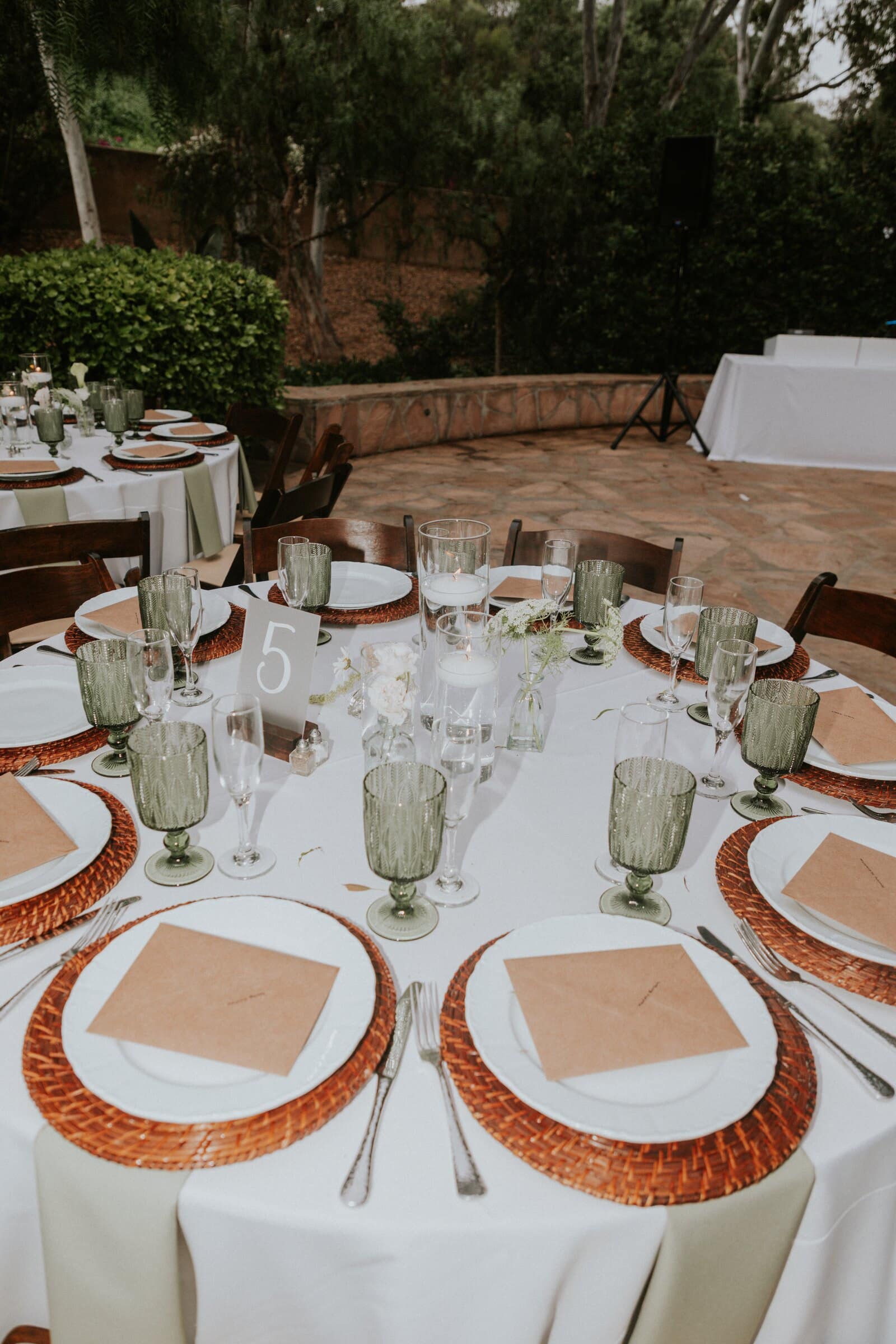 Reception tables set with green glassware and woven chargers