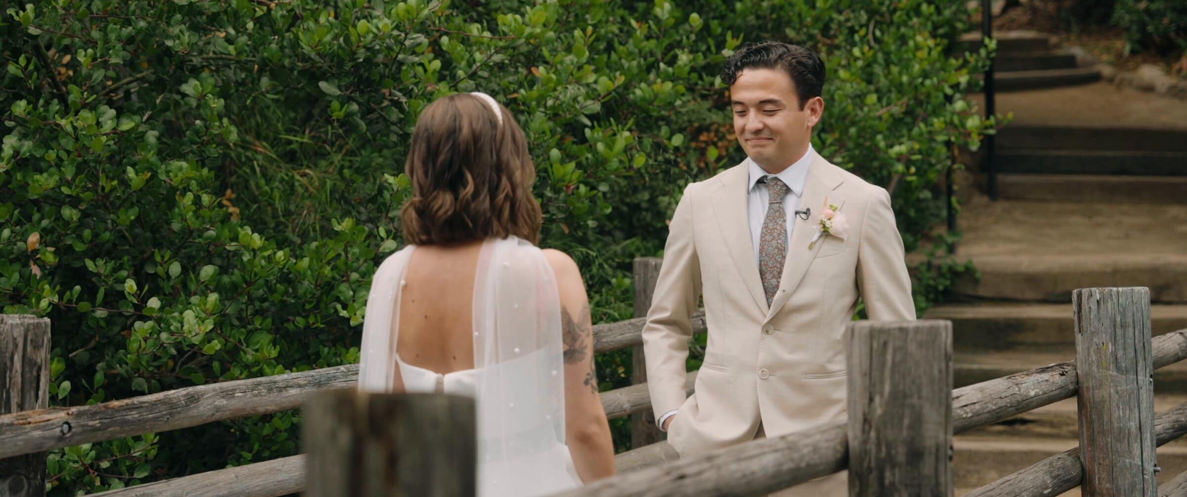 Caleb smiling at Megan during their first look beside a wooden fence