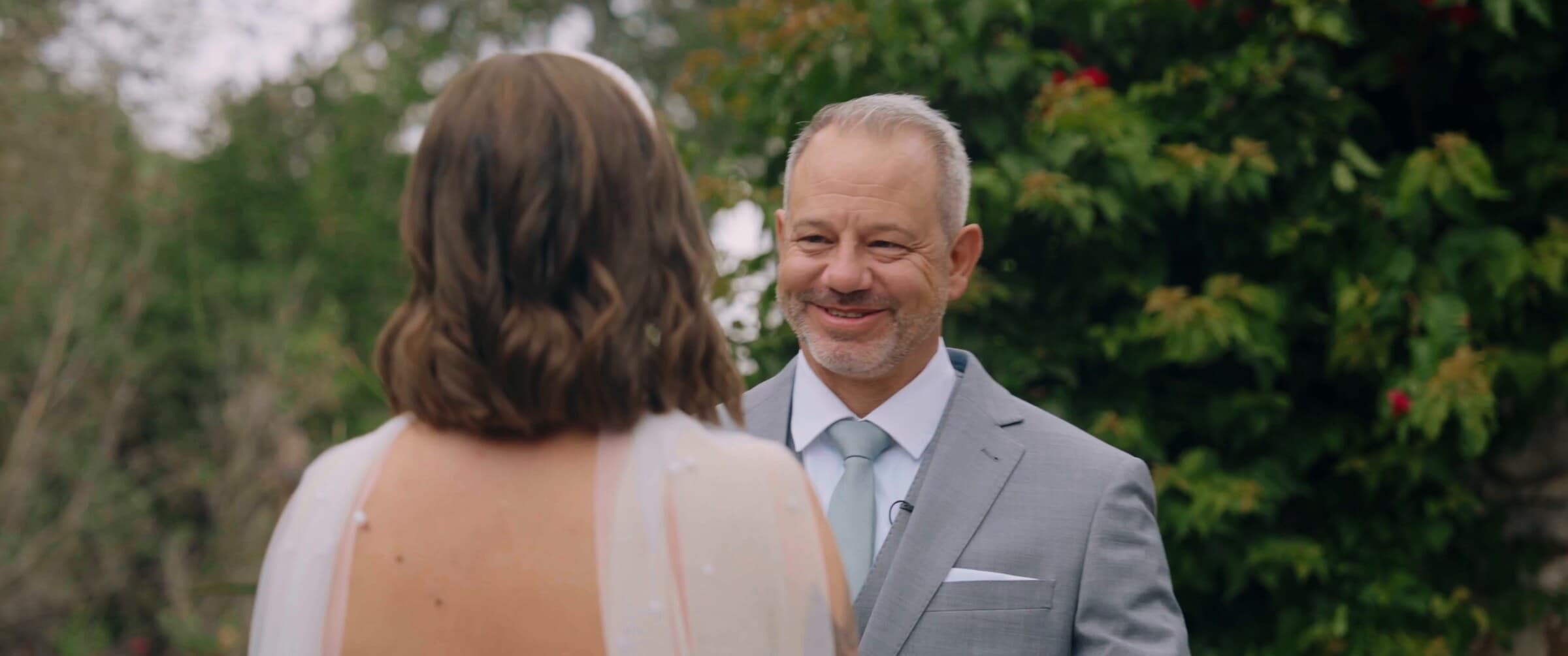 A man in a grey suit seeing Megan in her dress for the first time
