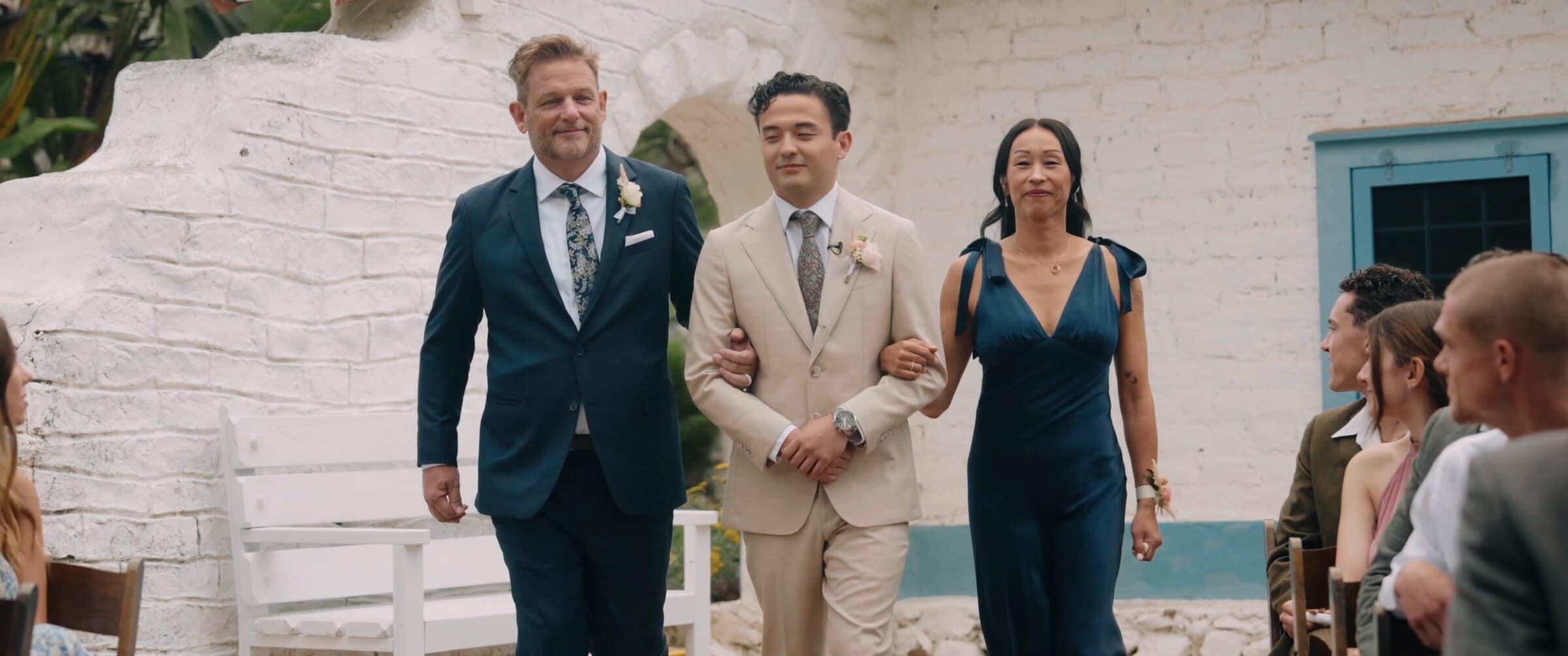Caleb walking down the aisle between family past a whitewashed wall
