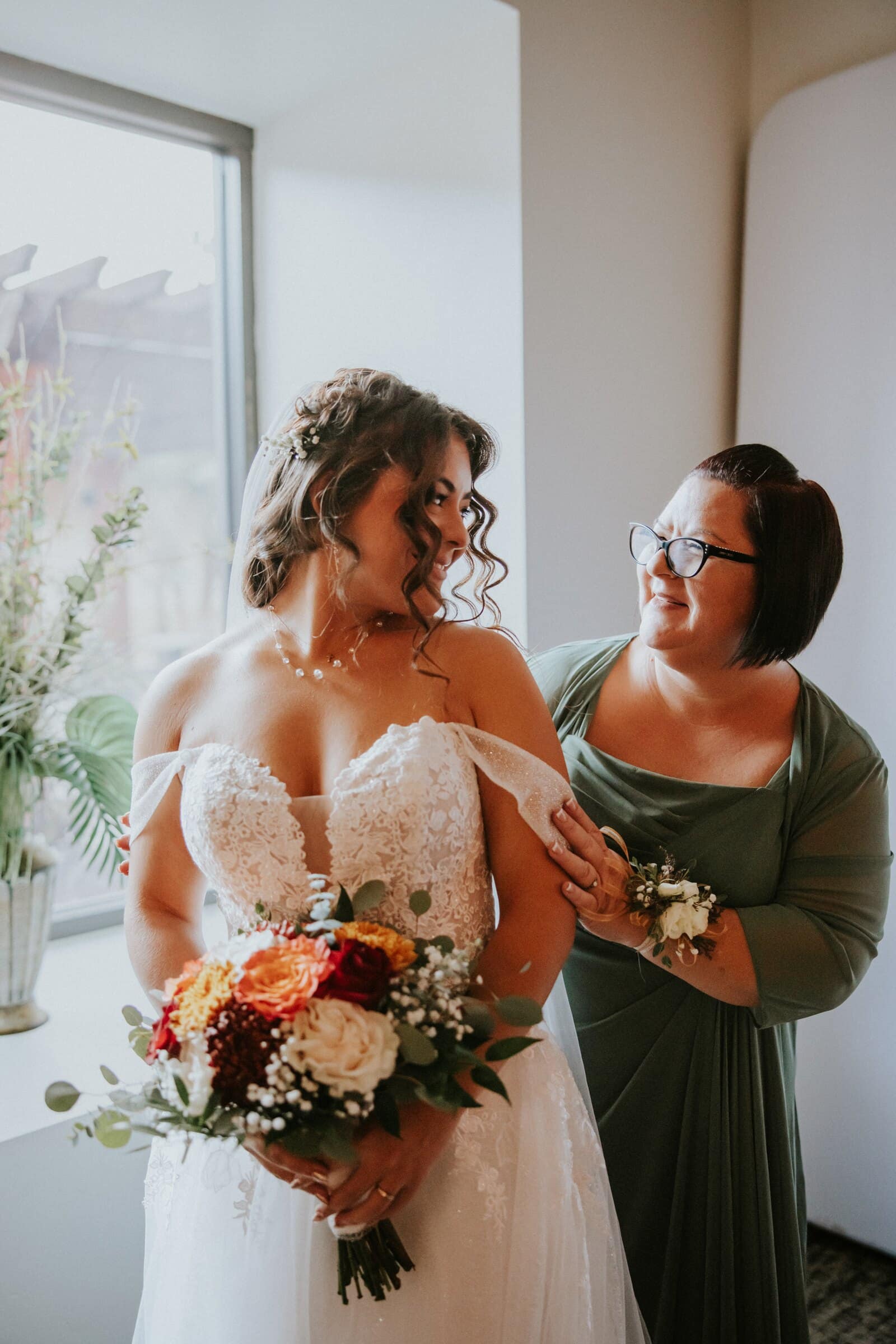 Natalie holding her bouquet as a woman in green adjusts her dress