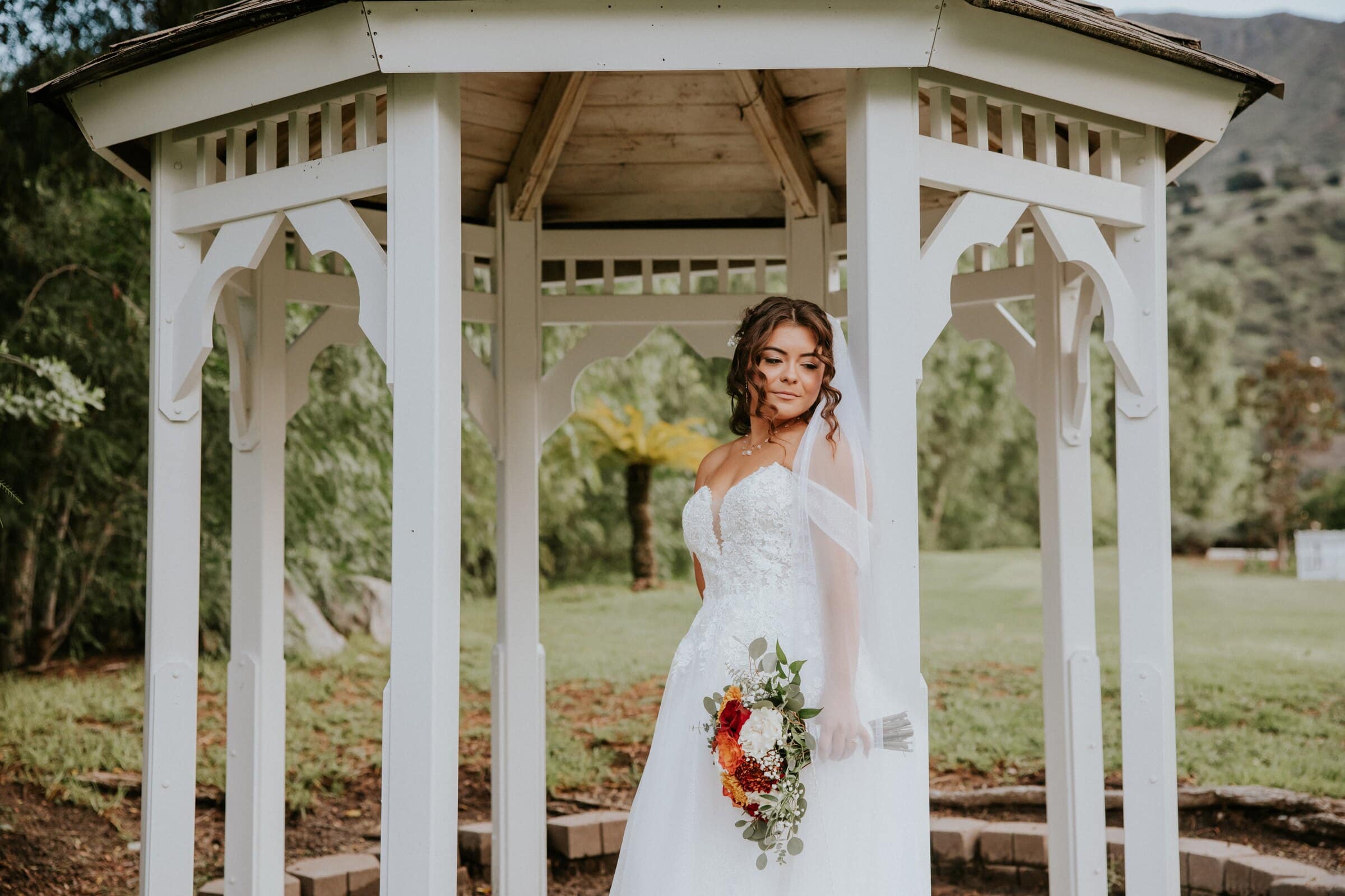 Natalie standing in a white gazebo with her bouquet