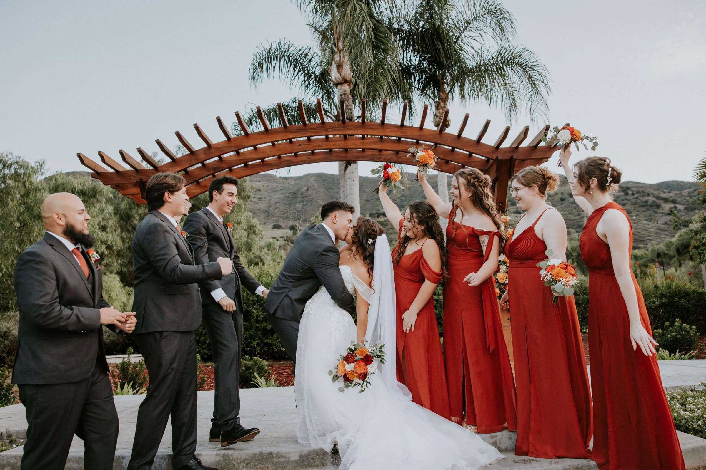 The wedding party cheering under the pergola as Natalie and David kiss