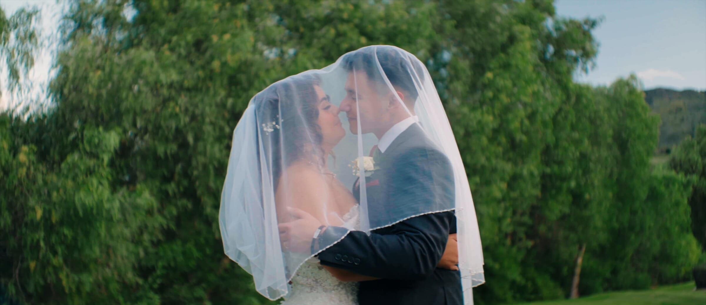 Natalie and David kissing beneath her veil with green hills behind them