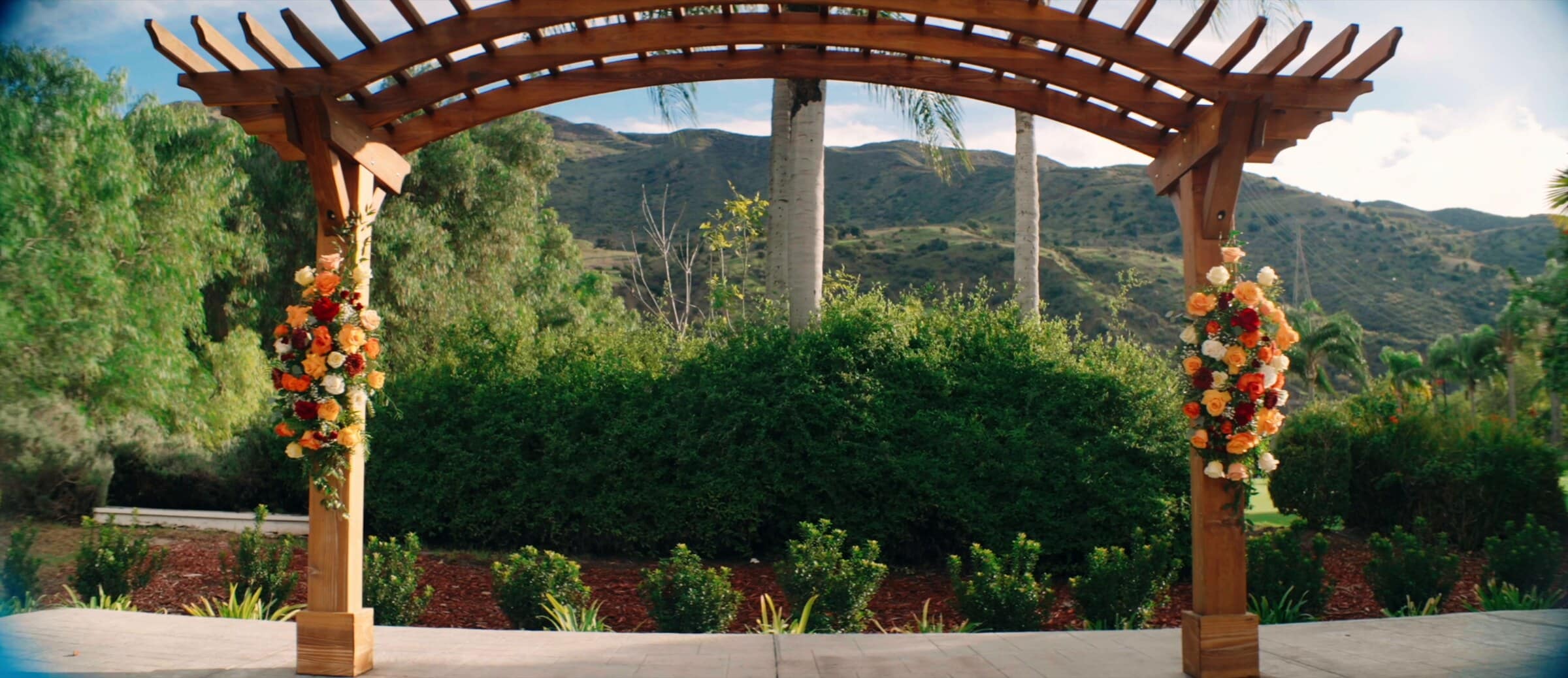 The wooden pergola dressed in orange and red flowers, hills beyond
