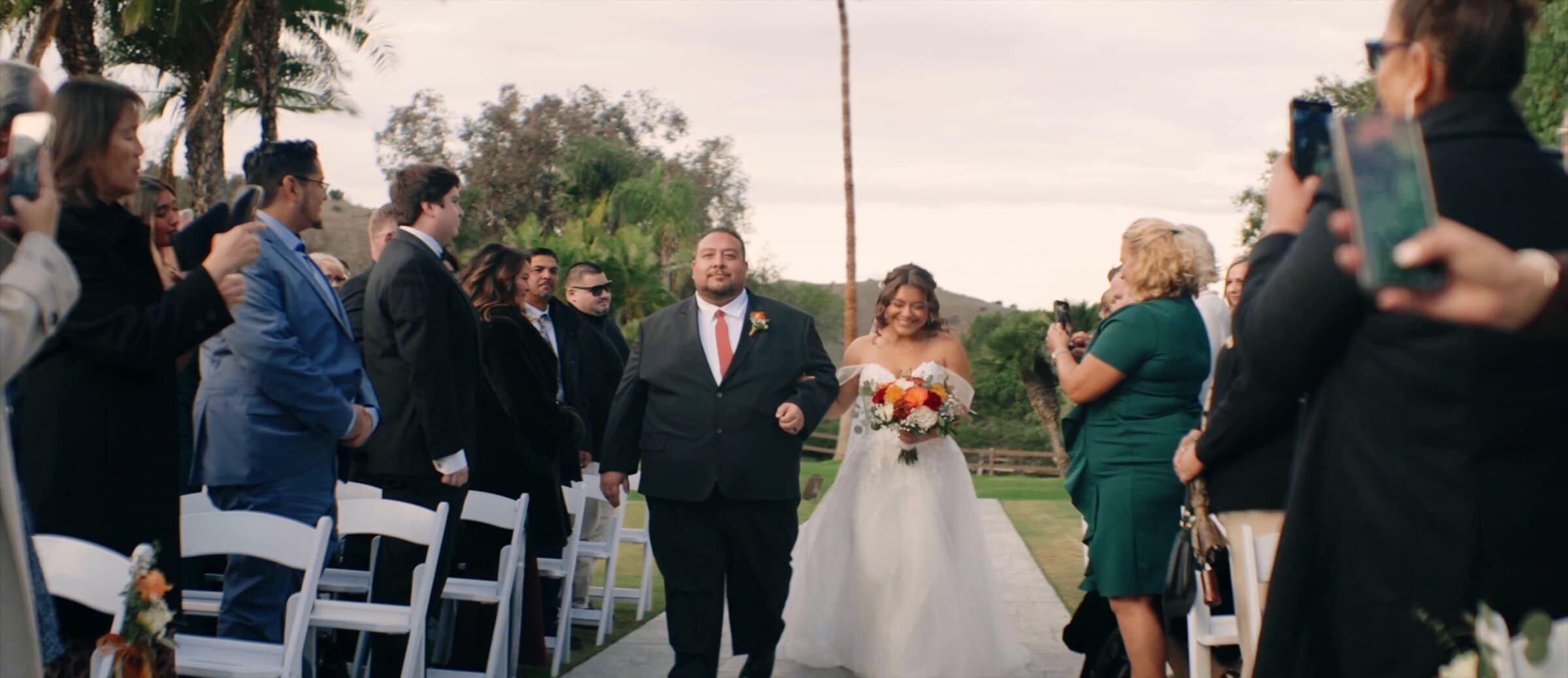Natalie walking down the aisle as guests raise their phones