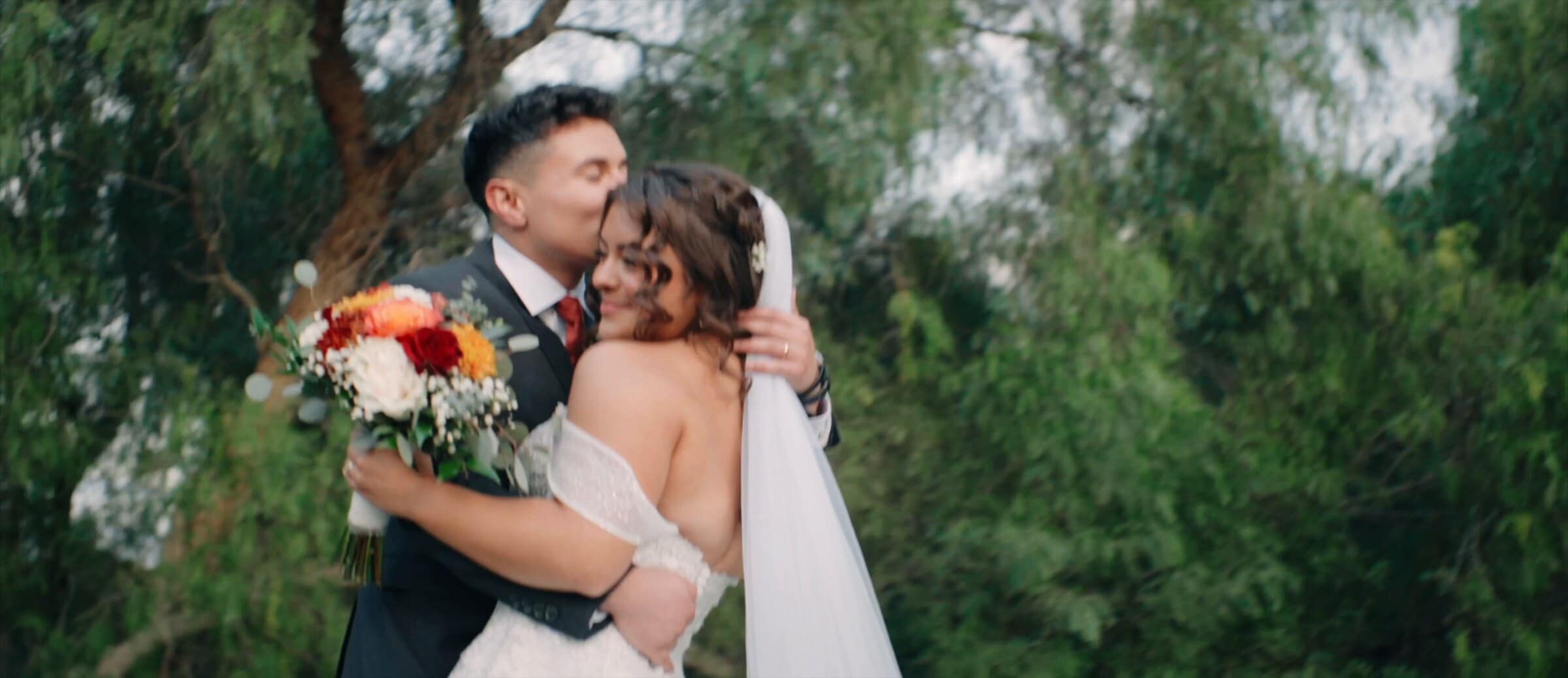 Natalie and David hugging, her bouquet of red and orange roses in hand