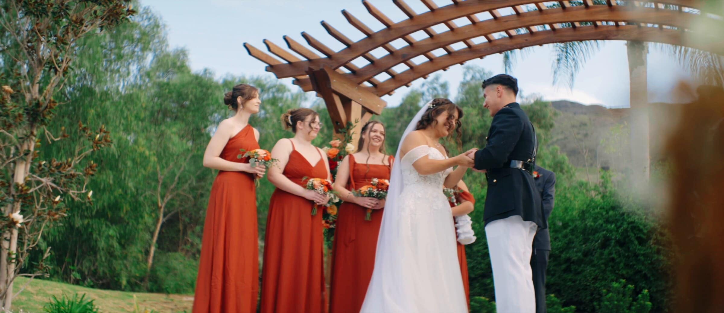 Natalie and David at the altar under the pergola, bridesmaids in rust red beside them