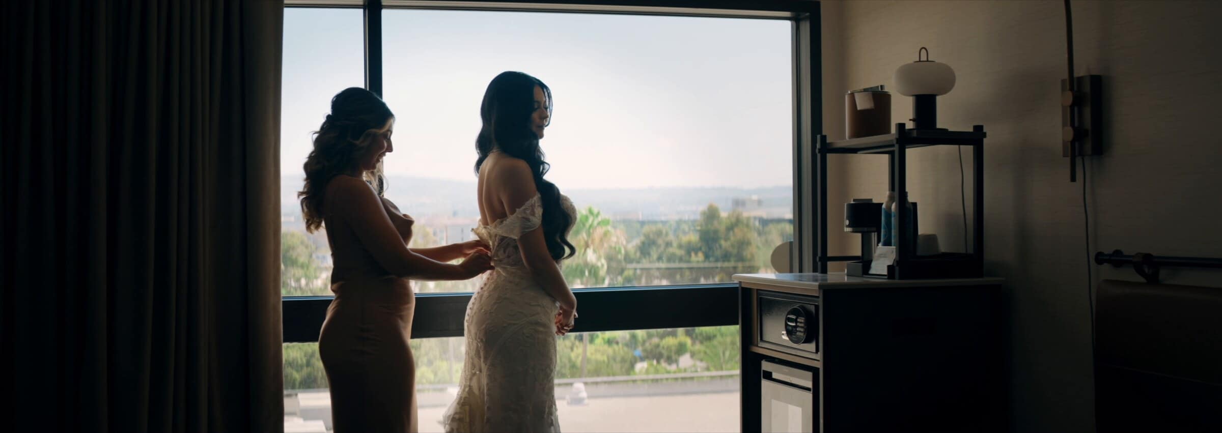 The bride being helped into her dress by a tall window