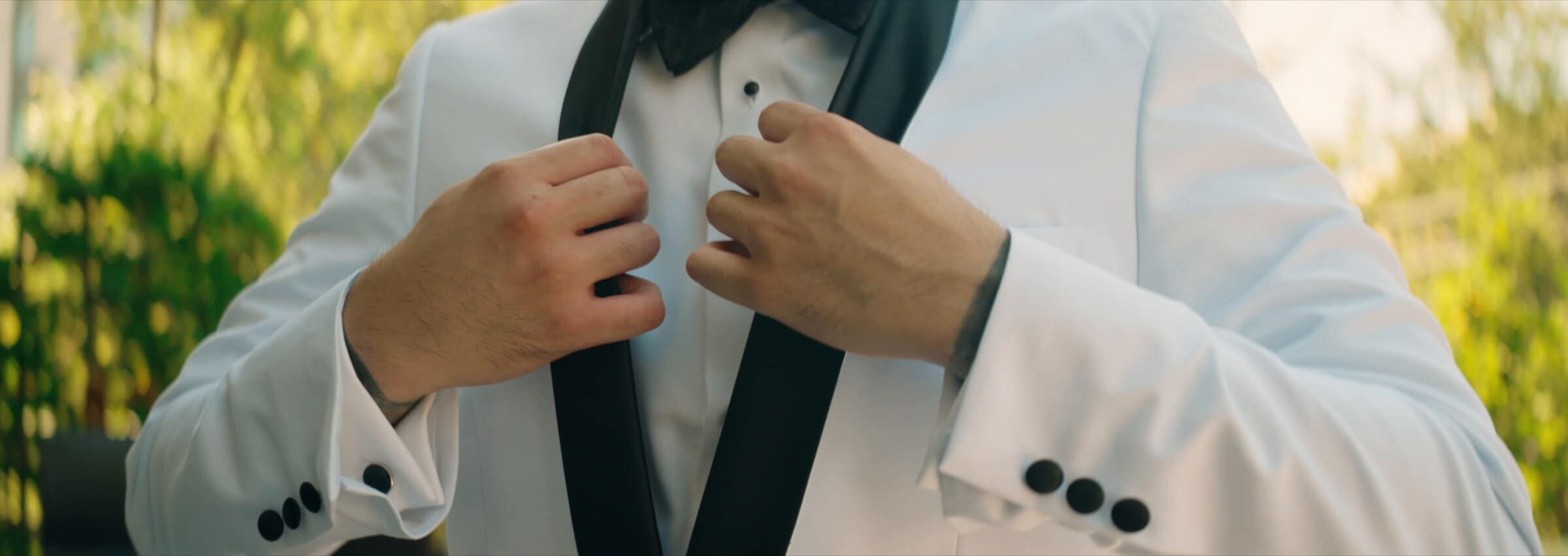 The groom buttoning his white tuxedo jacket